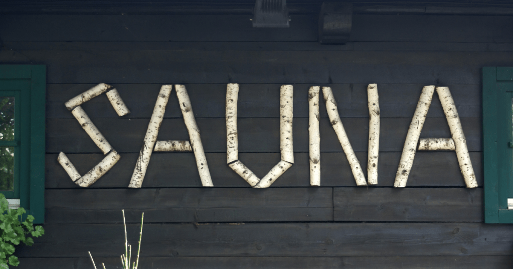 Wooden letters spelling “sauna” mounted on a rustic sauna wall made of birch
